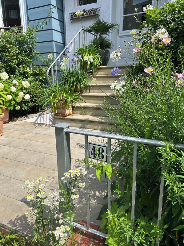 A residential property with a staircase leading to a door, surrounded by lush greenery and flowering plants. - Apartment in the Geteviertel - close to the city, trade fair, university, stadium and Weser cycle path (Schwachhausen)