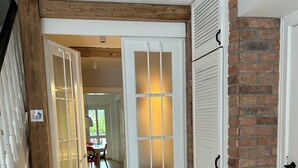 Un couloir doté d’un plancher en bois, d’une porte blanche avec des panneaux en verre dépoli et d’un mur en briques.