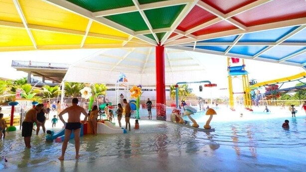 Un parc aquatique intérieur doté d’un espace central dédié aux jeux d’eau, entouré de divers toboggans et de structures de jeux aquatiques.