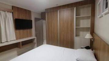 Un dormitorio con cama, televisor montado en la pared, armario y mesita de noche con lámpara.