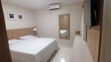 Een hotelkamer met een bed, nachtkastje, lamp, airconditioning en een spiegel, plus een televisie.