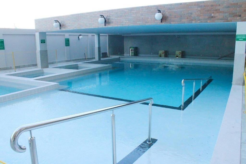A swimming pool with a metal safety railing, a brick wall, and a tiled floor.