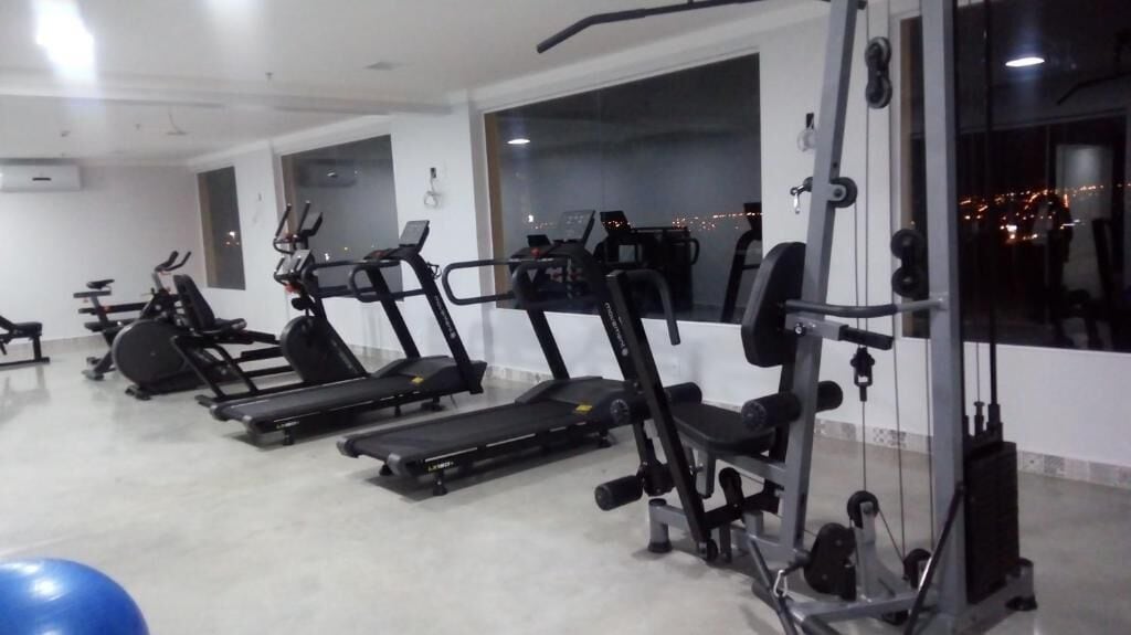Un gimnasio con cintas de correr, máquinas de pesas y un ventanal grande.