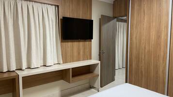 Un dormitorio con una cama, un televisor montado en la pared, un armario de madera y un espejo.