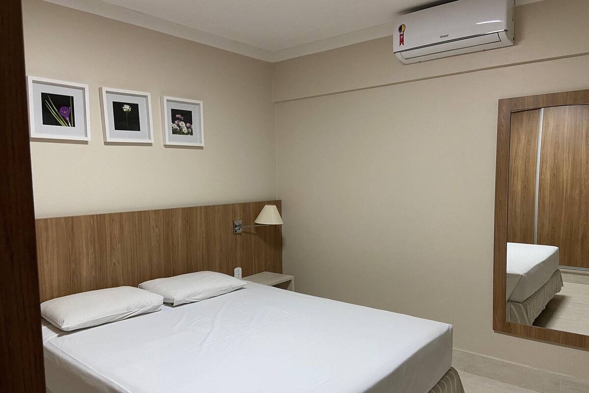 Habitación de hotel con cama, mesita de noche, lámpara y tres cuadros en la pared.