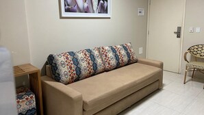 Un canapé beige agrémenté de coussins à motifs, un tableau encadré accroché au mur, une petite table en bois et une chaise en osier.