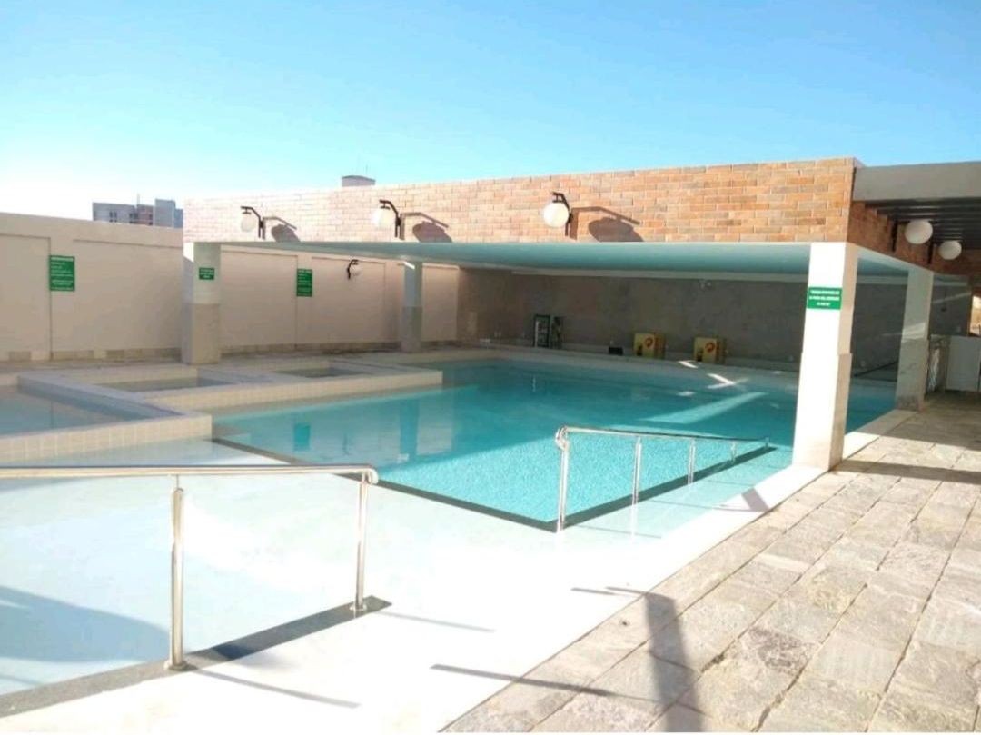 A swimming pool with a glass barrier, a brick wall, and a clear blue sky.