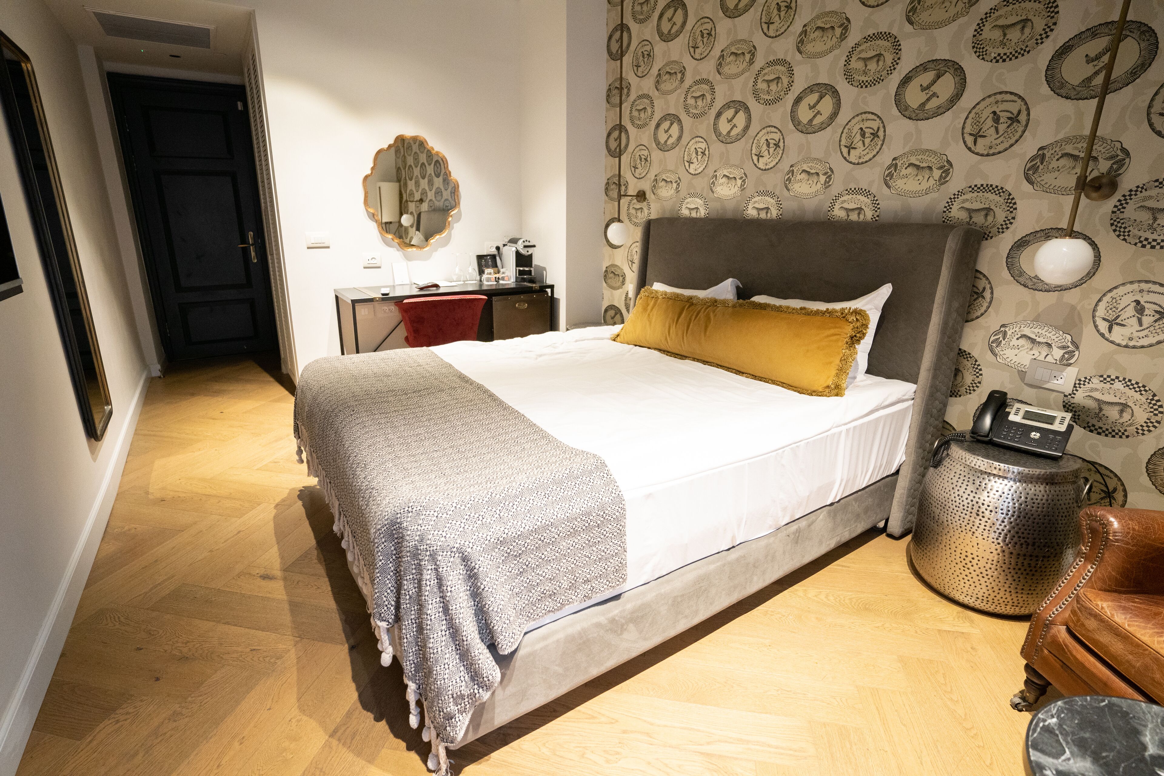 Een slaapkamer met een bed, een bureau, een stoel, een lamp en behang met een patroon.