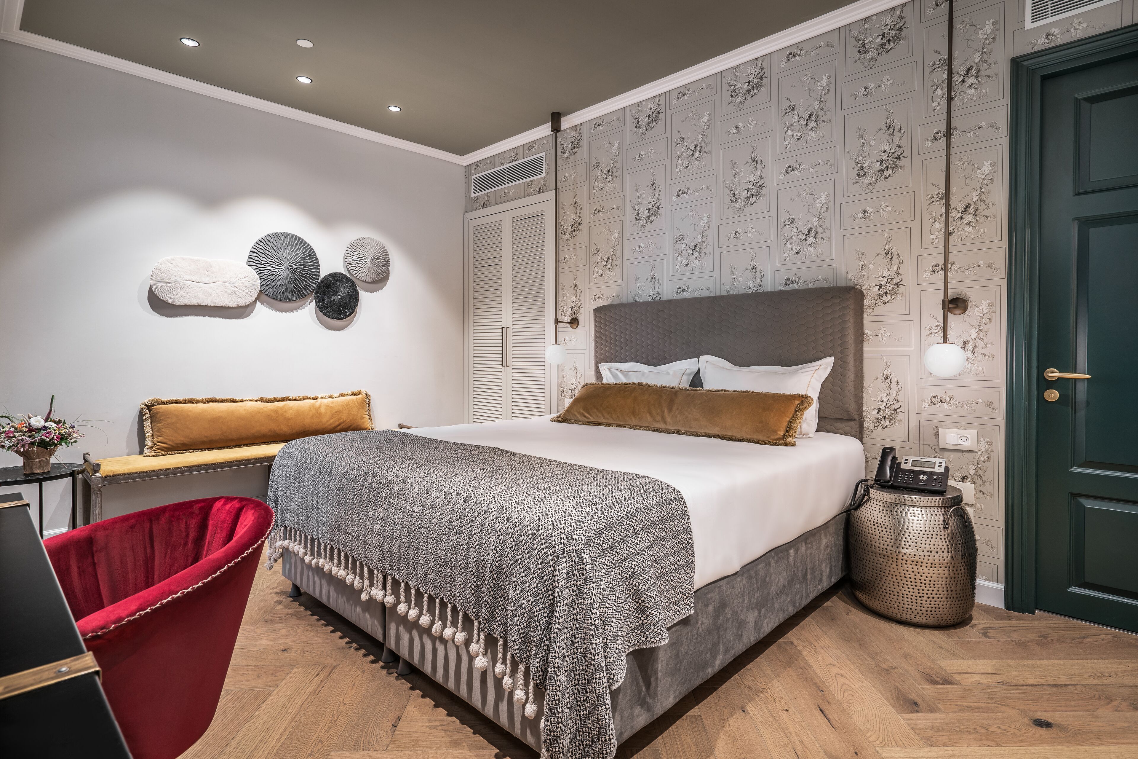 Un dormitorio con cama, una silla roja, una mesita de noche con lámpara y una pared decorada con arte mural.