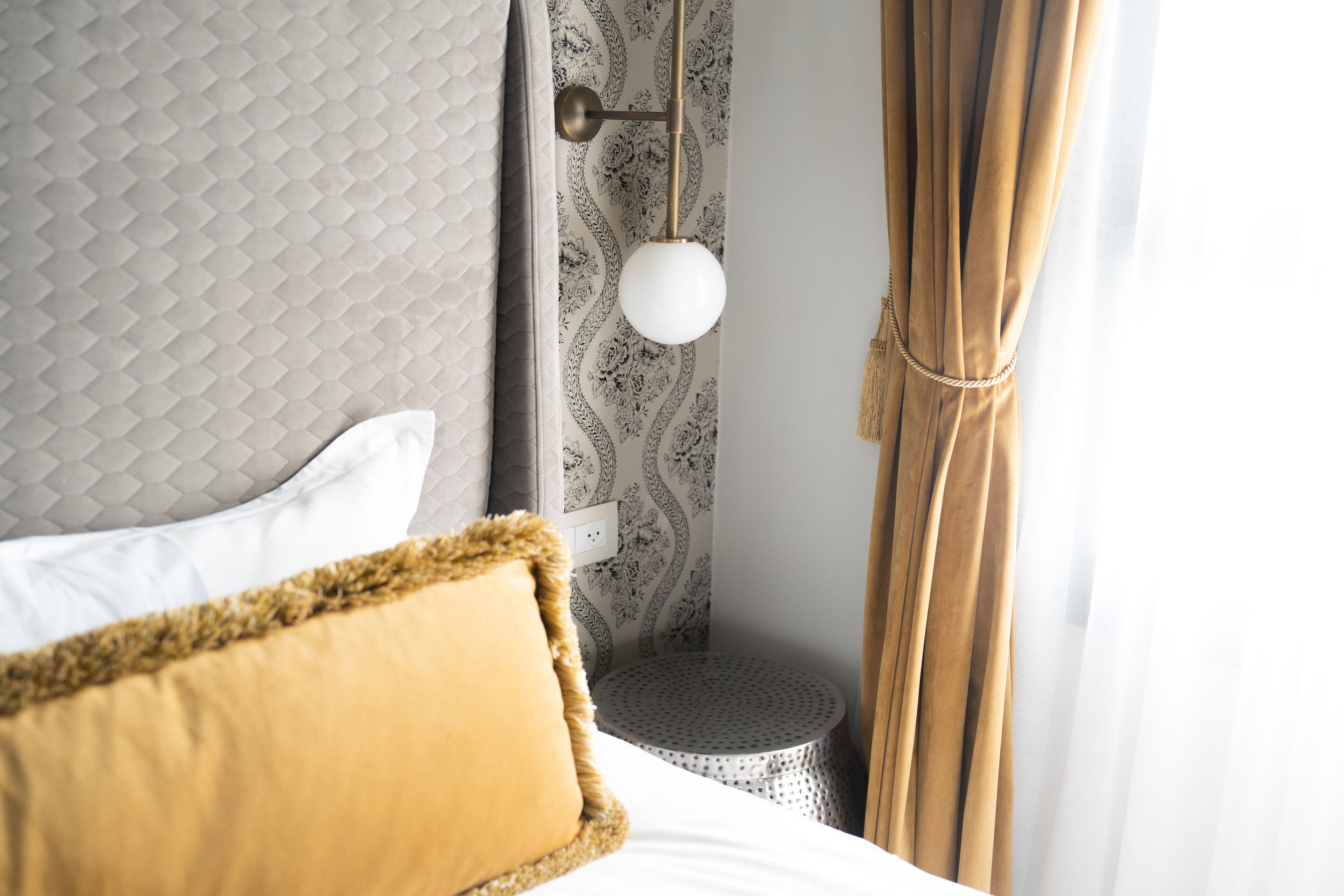 A neatly made bed with a fluffy pillow, a bedside table with a lamp, and patterned wallpaper.