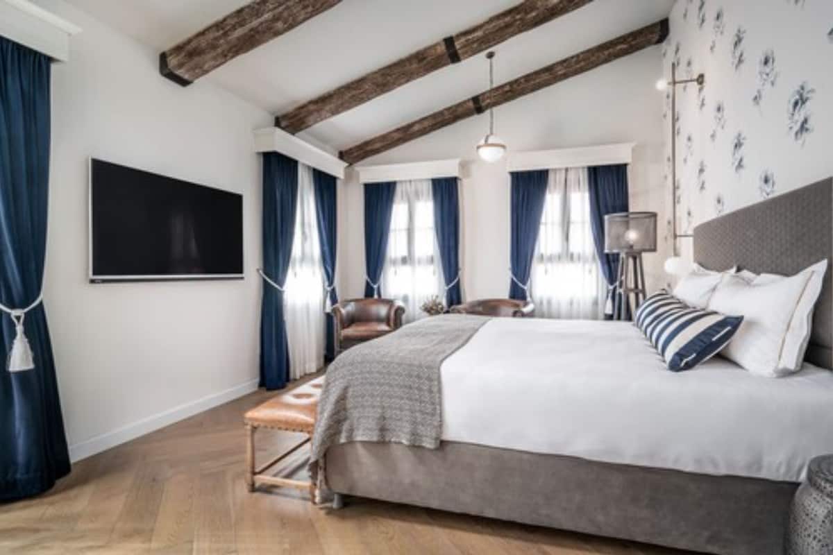 A bedroom with a large bed, wooden beams, a flat-screen TV, and a desk with a chair.
