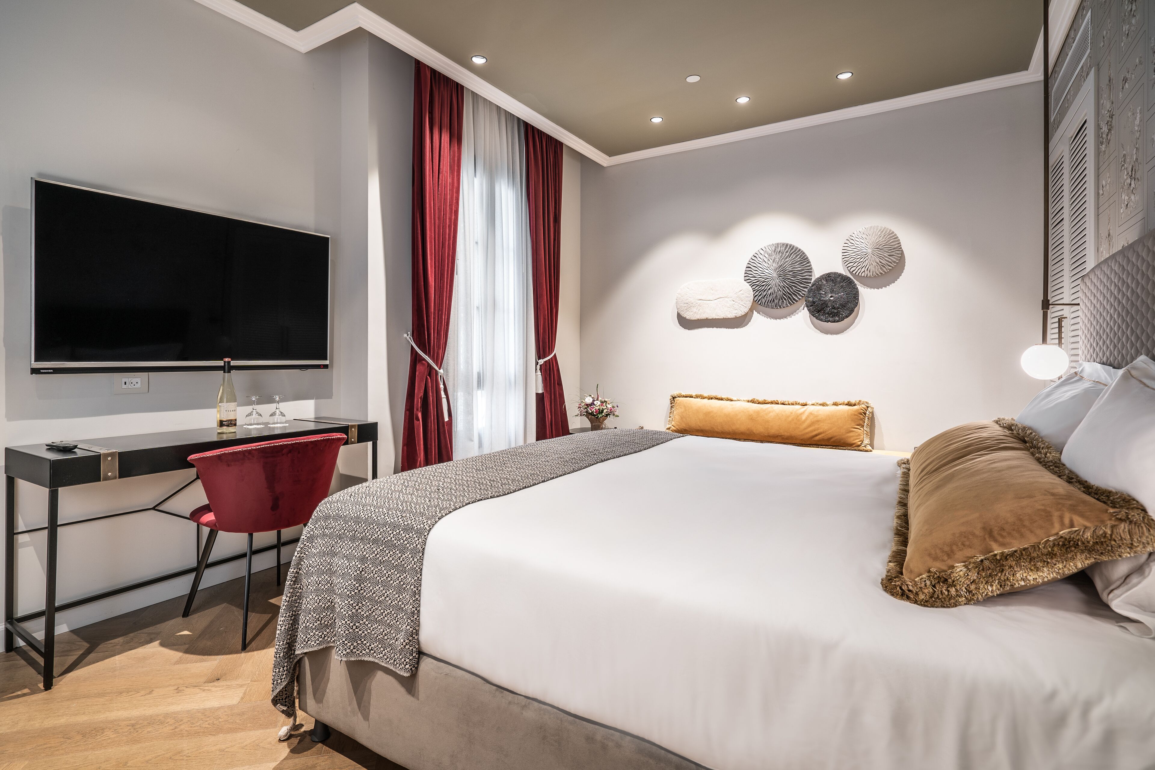 Une chambre moderne avec un grand lit, un bureau avec une chaise, un téléviseur à écran plat et des œuvres d’art décoratives au mur.