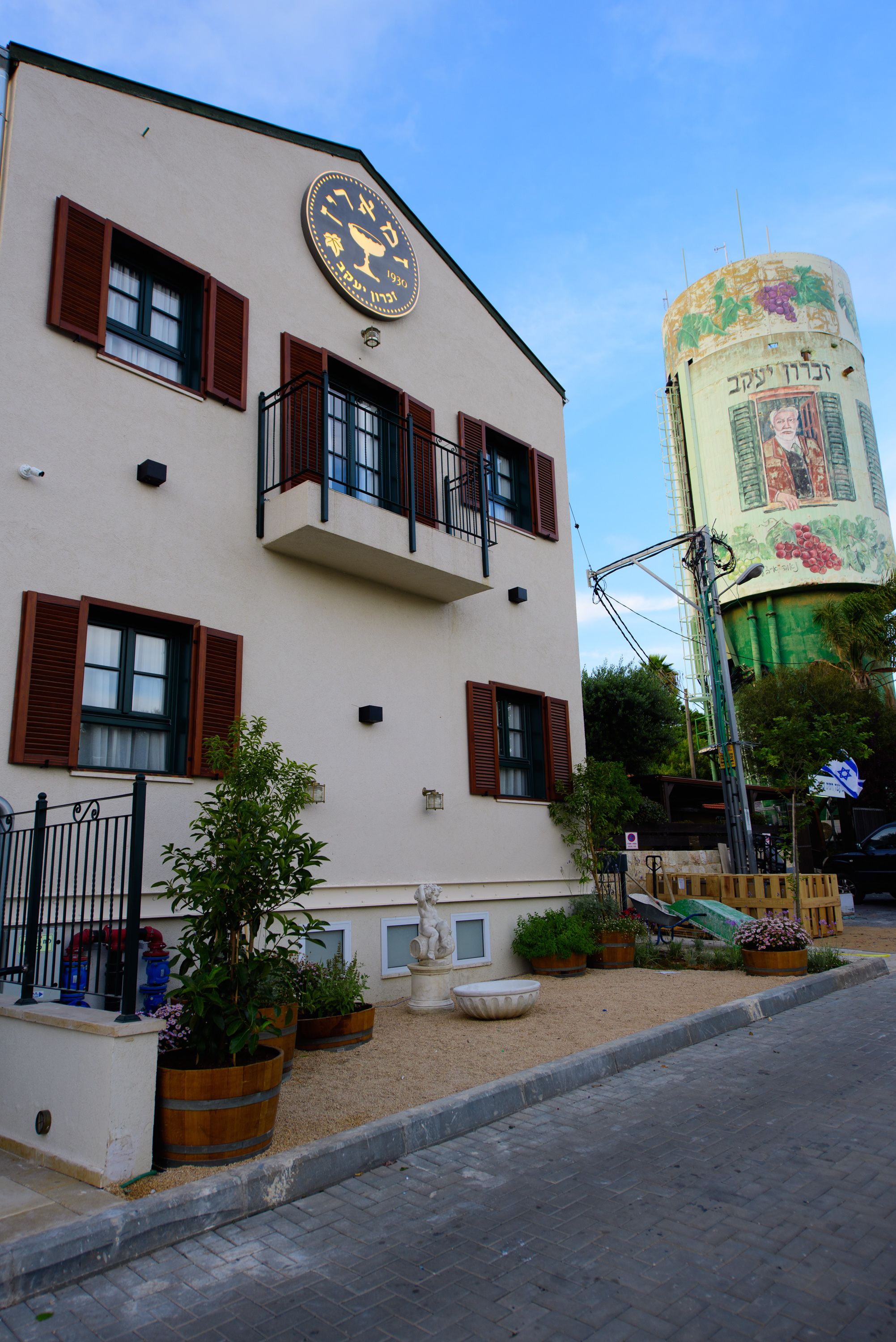 A building with a clock, a water tower, and a street with potted plants.