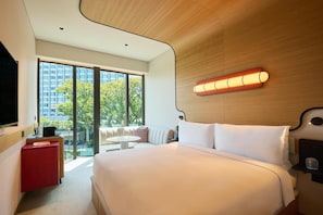 Una habitación de hotel moderna con una cama grande, un escritorio, una silla, una mesita y un televisor.