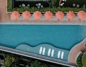 An aerial view of a swimming pool with surrounding lounge chairs and umbrellas, surrounded by greenery.