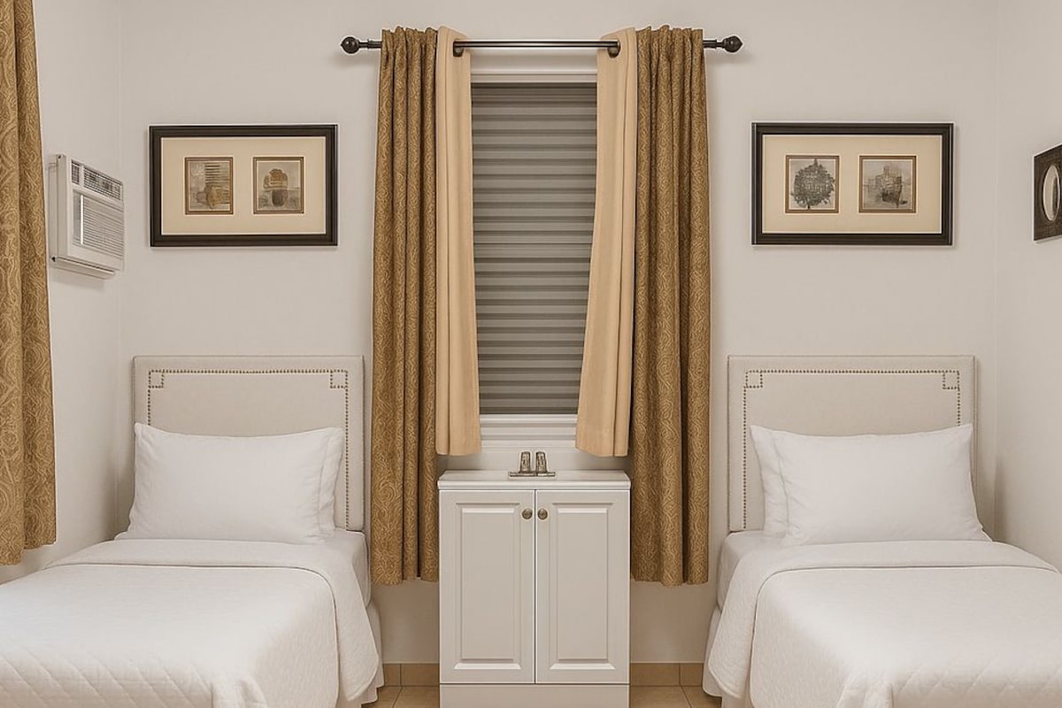 Una habitación de hotel con dos camas, un mueble blanco pequeño y dos cuadros en las paredes.