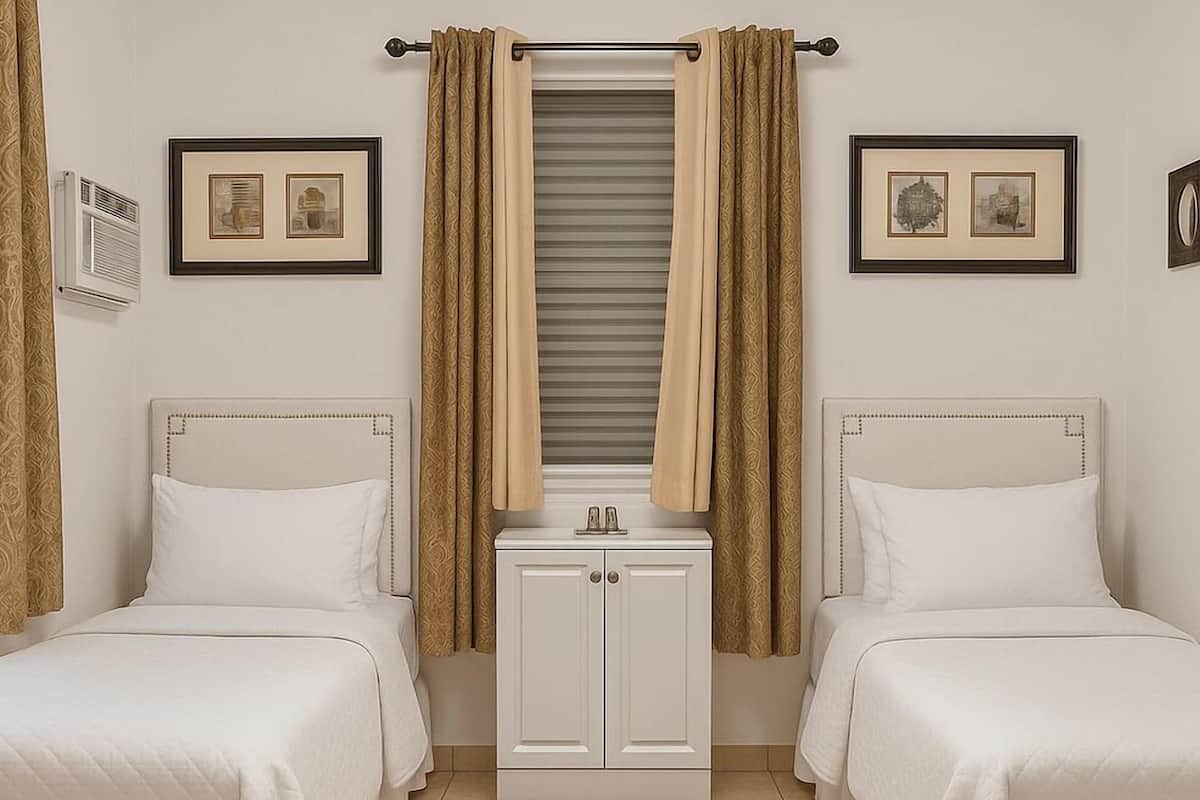 Una habitación de hotel con dos camas, un mueble blanco pequeño y dos cuadros en las paredes.