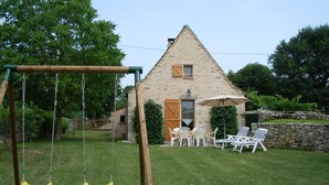 Een stenen huis met een puntig dak, een schommel en buitenmeubilair.