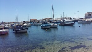 Un puerto deportivo con varias embarcaciones amarradas, agua cristalina y edificios al fondo.