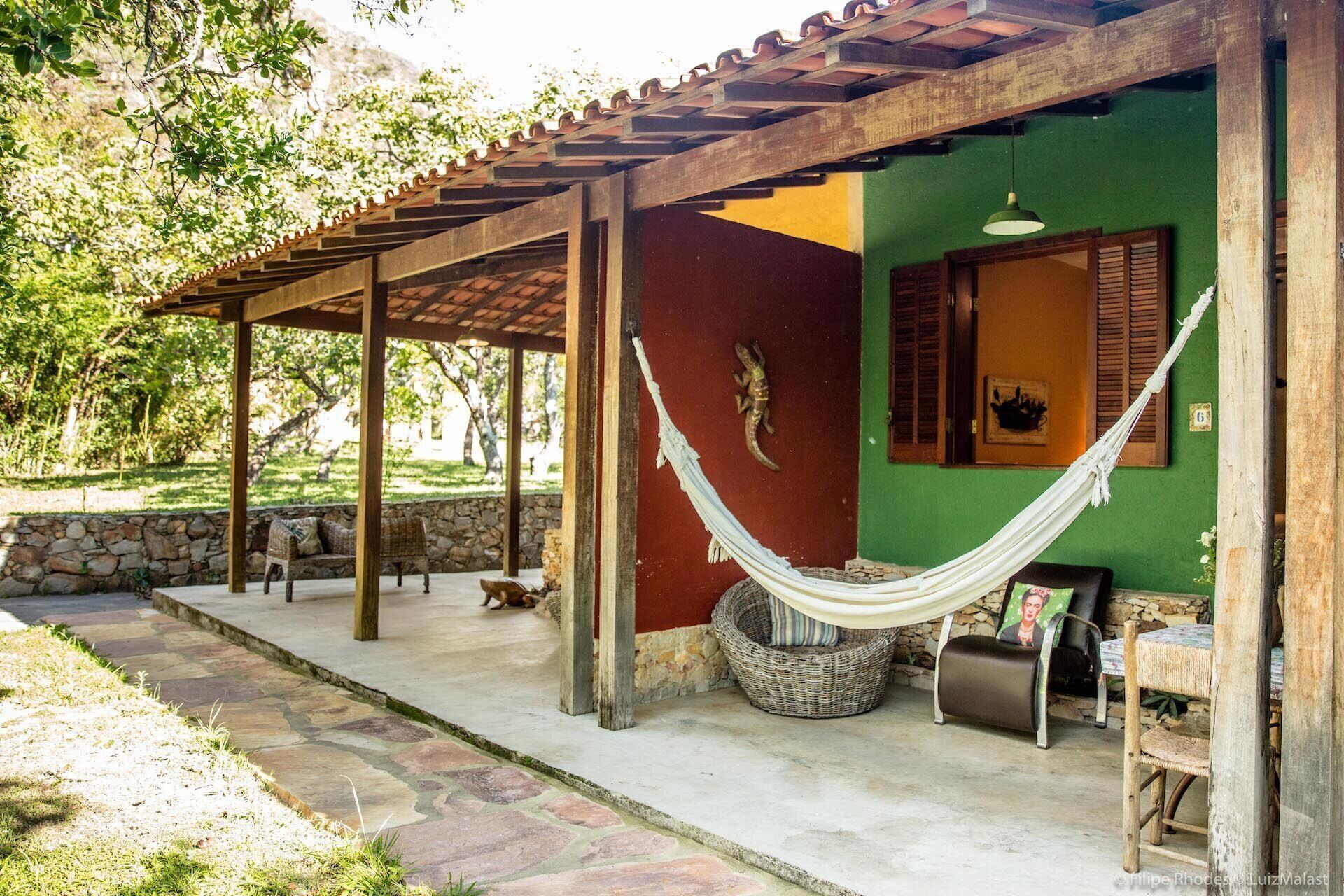 Uma área de estar coberta ao ar livre com uma rede, paredes de pedra e uma parede verde com uma porta.