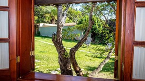 Una puerta de madera abierta que da a un jardín con un árbol, césped y un edificio al fondo.