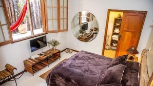 Un dormitorio con una cama grande, televisión, escritorio de madera, espejo y armario.