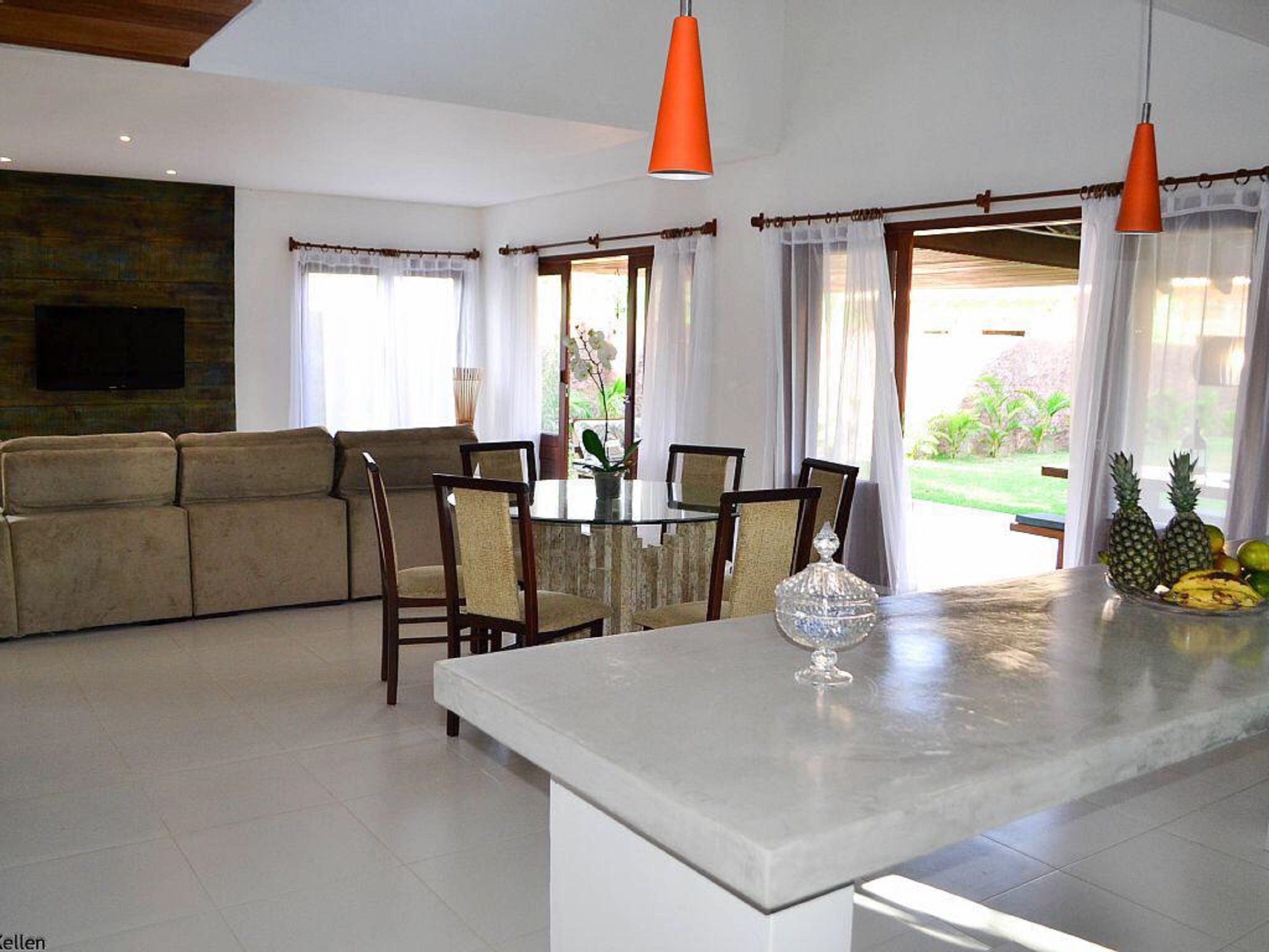 A modern living room with a sofa, dining table, chairs, and a kitchen island with fruit.