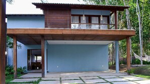 A modern two-story house with a covered patio area and a concrete driveway. - Casa Palmeira Condomínio em Trancoso (Porto Seguro)
