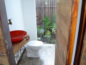 Casa de banho compacta com sanita branca, lavatório vermelho e prateleira de madeira.