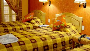 Habitación de hotel con dos camas, cada una con colcha a cuadros, almohadas y una mesita de noche con lámpara y teléfono.