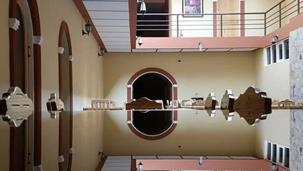 Una habitación simétrica con un espejo central que refleja el espacio, una escalera que conduce a un nivel superior y una puerta con un ventanal circular.