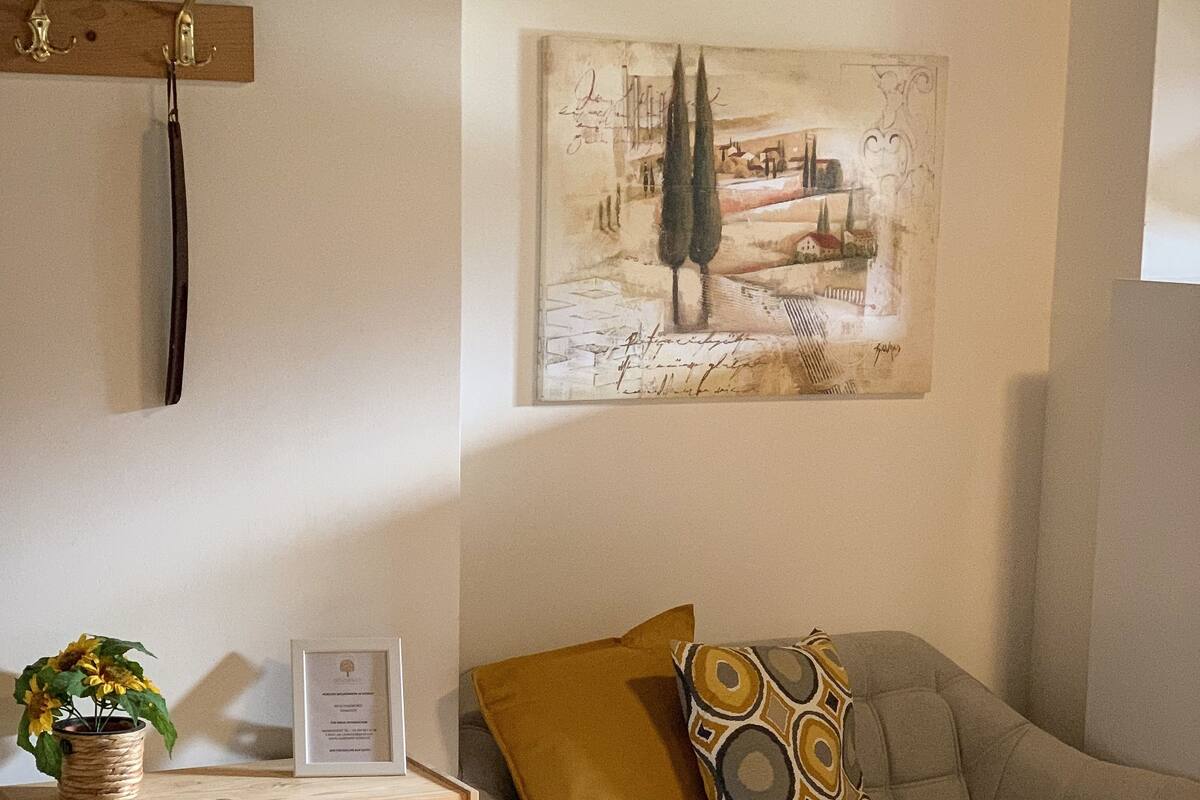 A room with a wooden dresser, a light grey sofa with patterned cushions, and a framed picture on the wall.