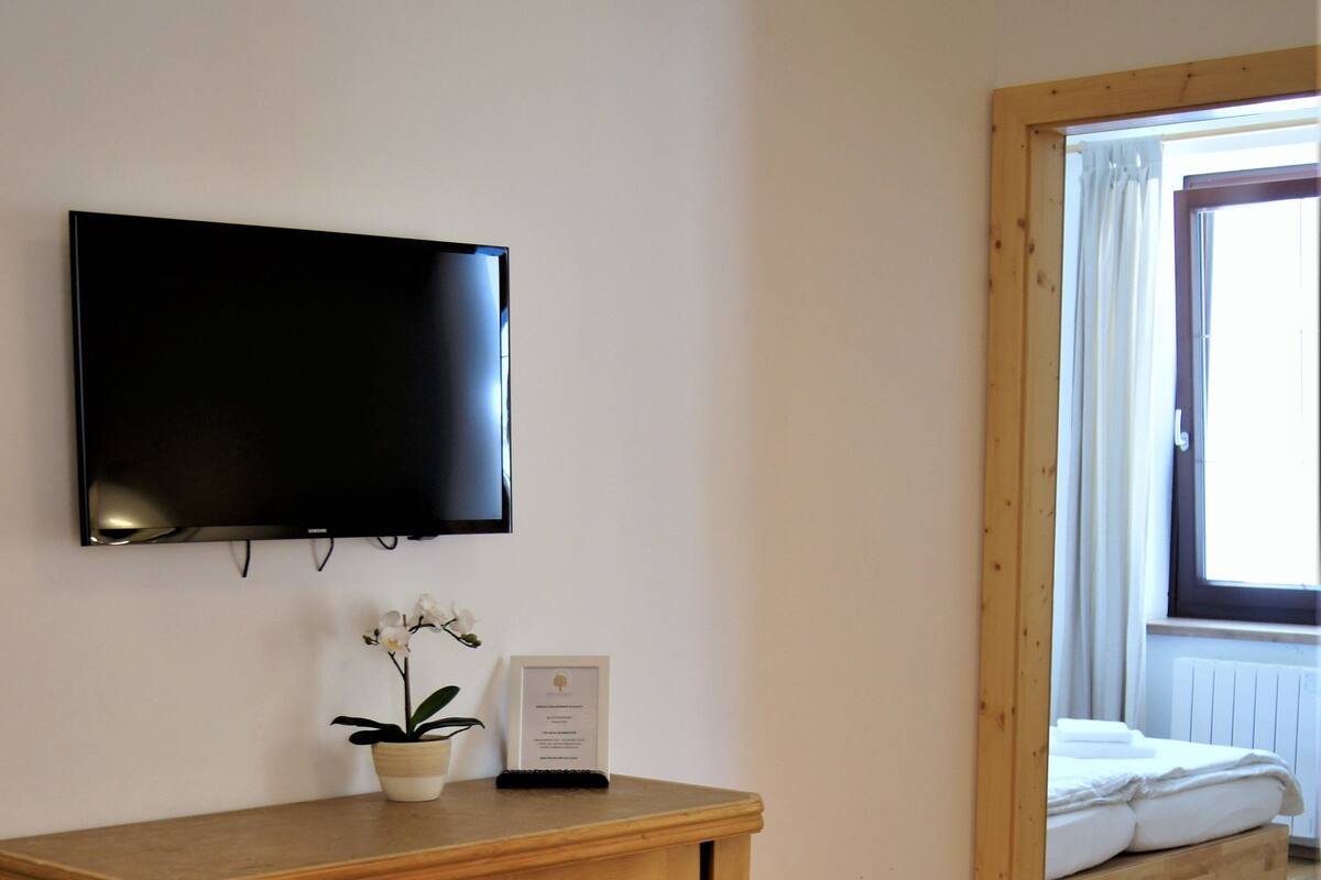 A wooden cabinet with drawers, a flat-screen TV mounted on the wall, and a window with curtains.
