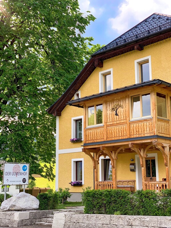 A two-story building with a balcony, a sign for 'DER ULMENhof Restaurant Das Horn', and a stone wall in the foreground. - COOEE alpin Apartments Gosau (Gosau)