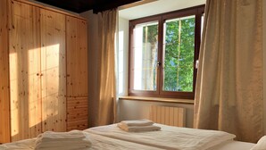 A room with two beds, wooden walls, a window with curtains, and a radiator. - Der Ulmenhof (Gosau)