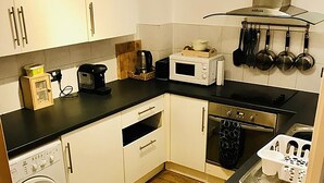 A compact kitchen with white cabinets, a microwave, a stove, and a washing machine. - Granary Mews (Crediton)