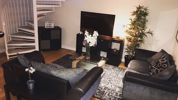 A modern living room with a staircase, a flat-screen TV, and a potted plant. - Granary Mews (Crediton)