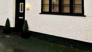 A two-story house with a black door, two windows with shutters, and a small light fixture above the door. - Granary Mews (Crediton)