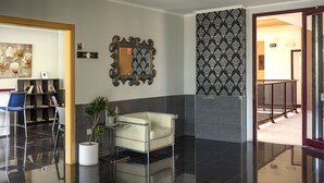 A modern lobby with a sofa, a potted plant, a bookshelf, and a mirror. - Aparthotel El Faro (Cullera)
