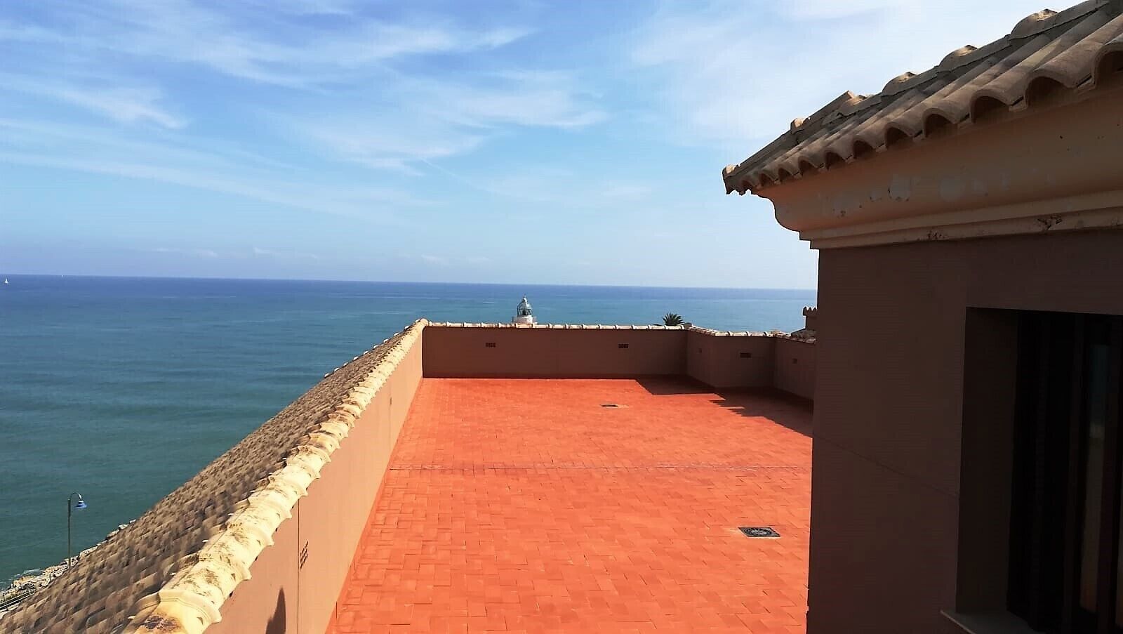 A rooftop terrace with a view of the sea, featuring a tiled floor and a stone wall.
