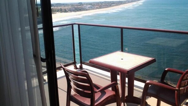 A balcony with a table and chairs overlooking a beach and ocean. - Aparthotel El Faro (Cullera)
