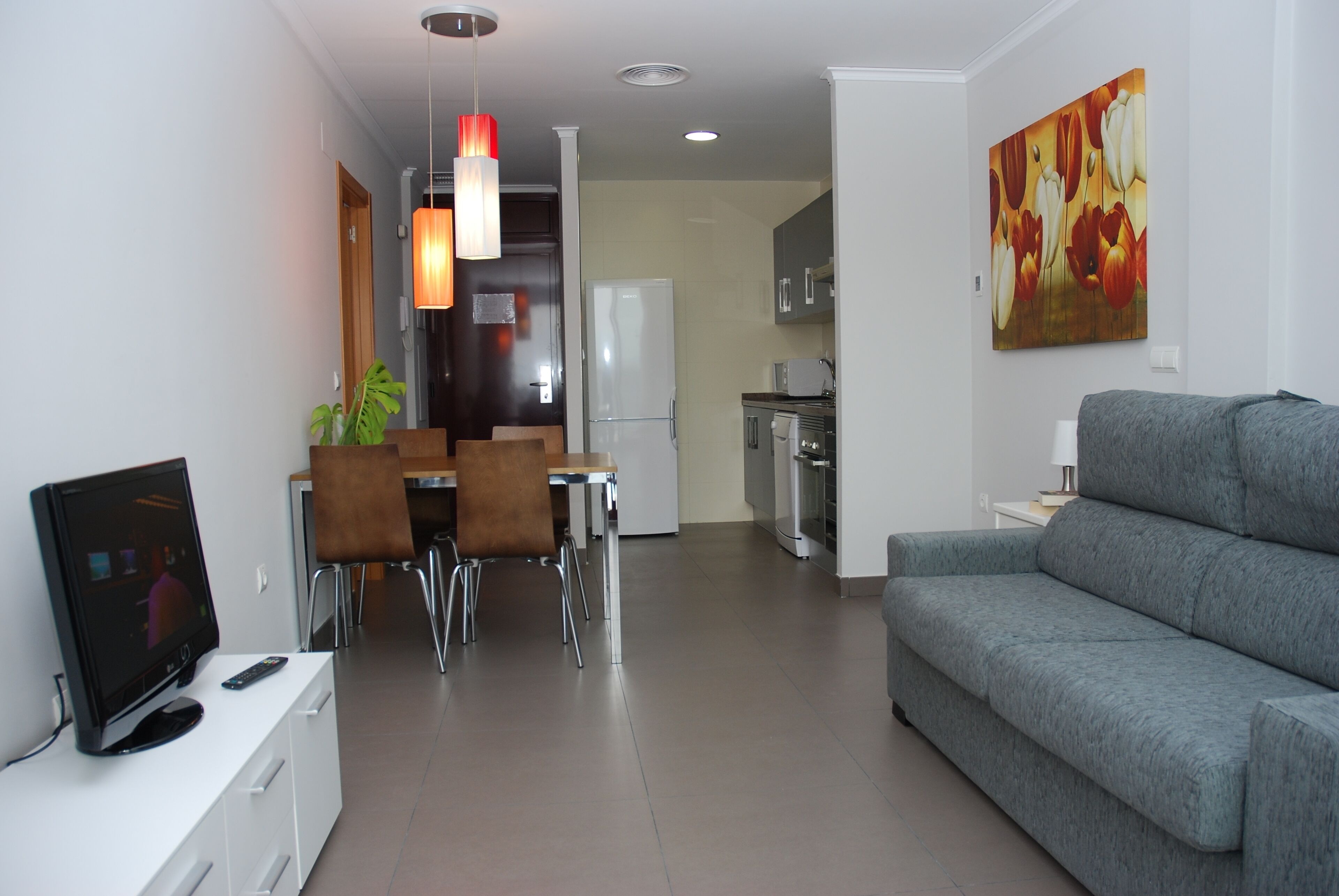 A modern living room with a grey sofa, a flat-screen TV, and a dining area with a table and chairs.