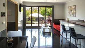 A modern hotel lobby with a glass door leading to an outdoor seating area, a reception desk, and a bar area with high stools. - Aparthotel El Faro (Cullera)