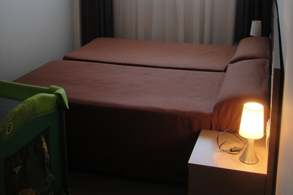 A small hotel room with a single bed, a nightstand with a lamp, and a window with curtains.