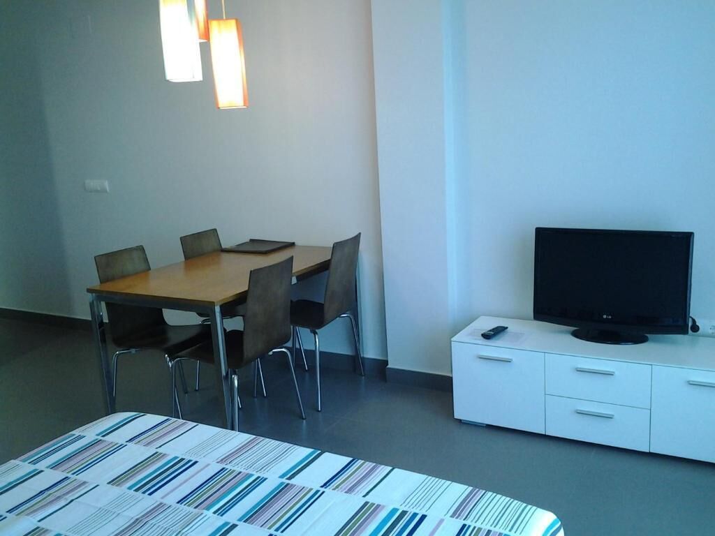 A hotel room with a bed, a dining table with chairs, a TV on a cabinet, and pendant lights.