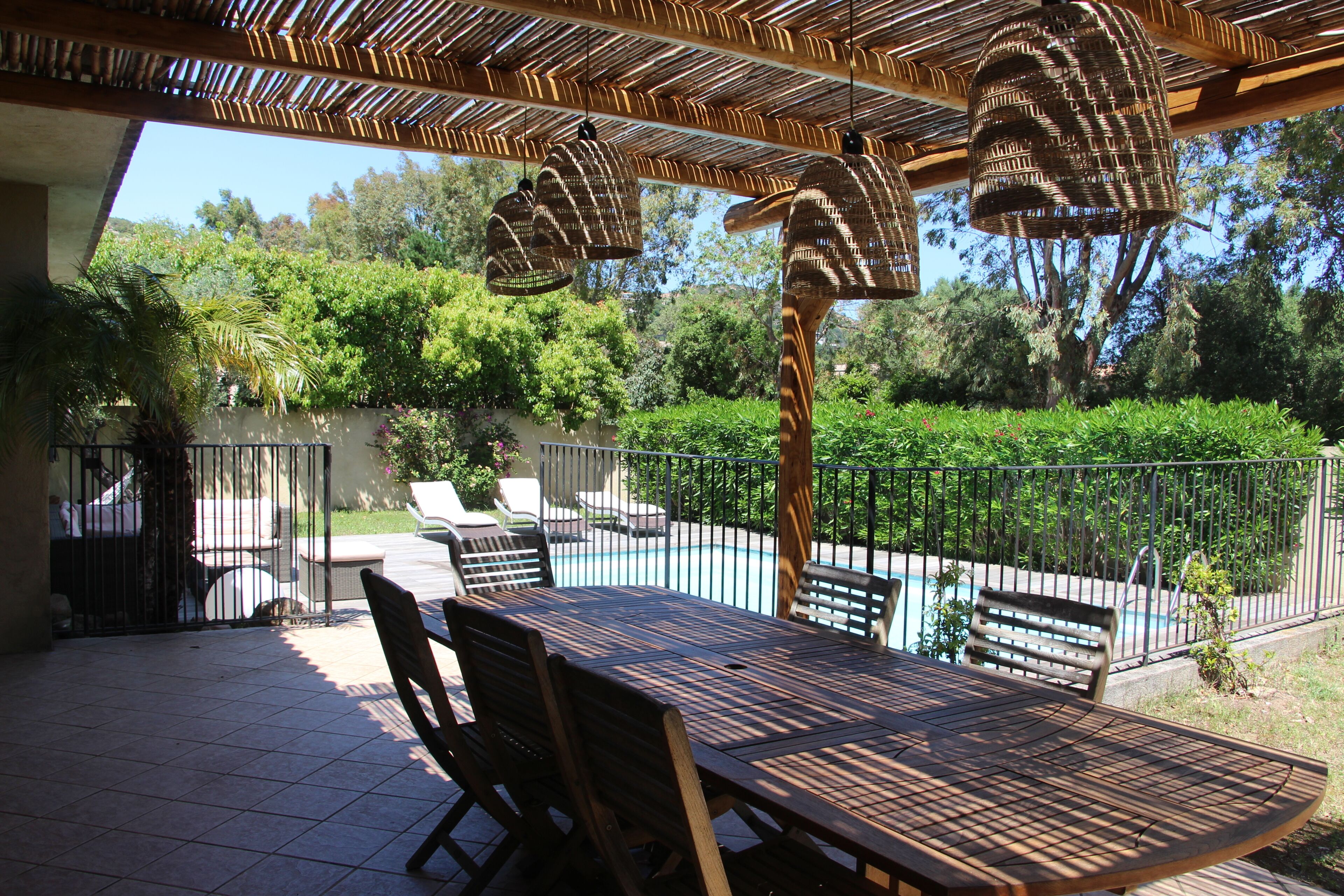 Eine Außenpatio mit Pool, Holzmöbeln und hängenden Korblampen.