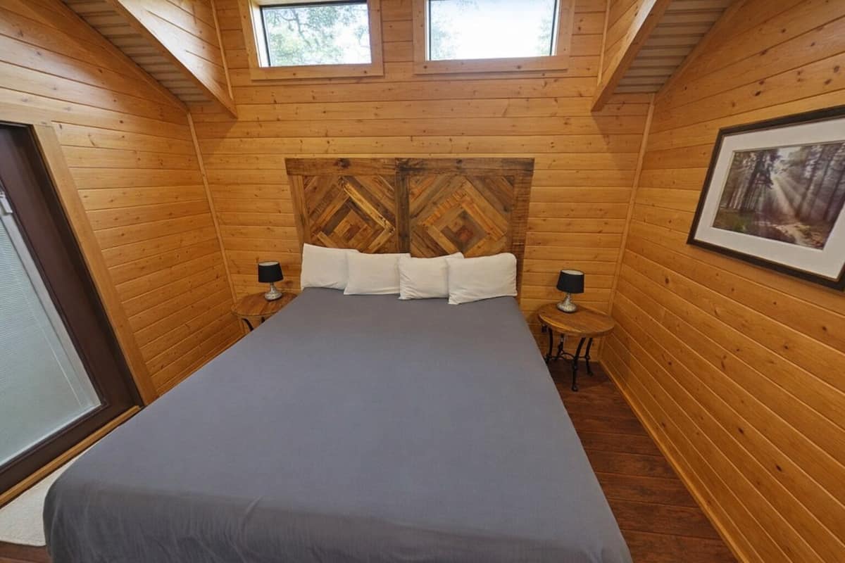 A wooden cabin bedroom with a bed, two bedside tables, and a large window.