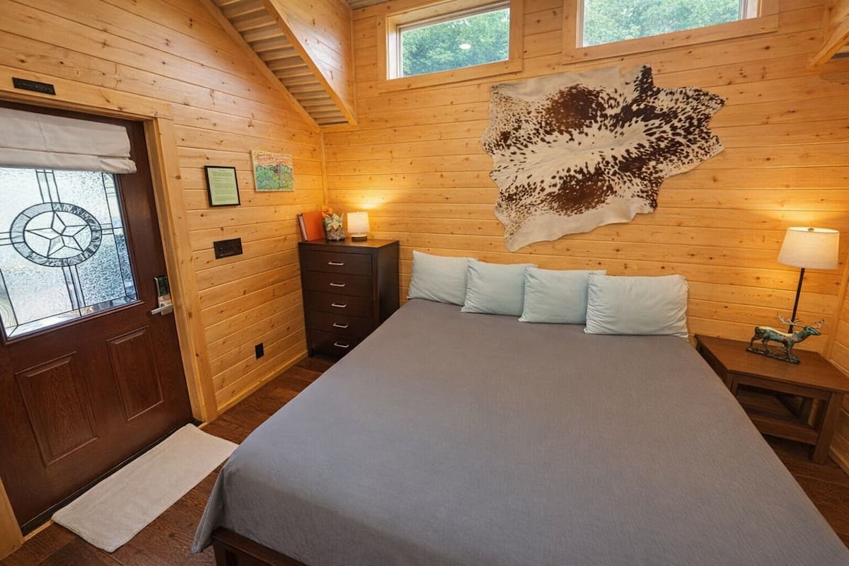 A wooden room with a bed, a dresser, a wall-mounted animal hide, and a window with a star design.