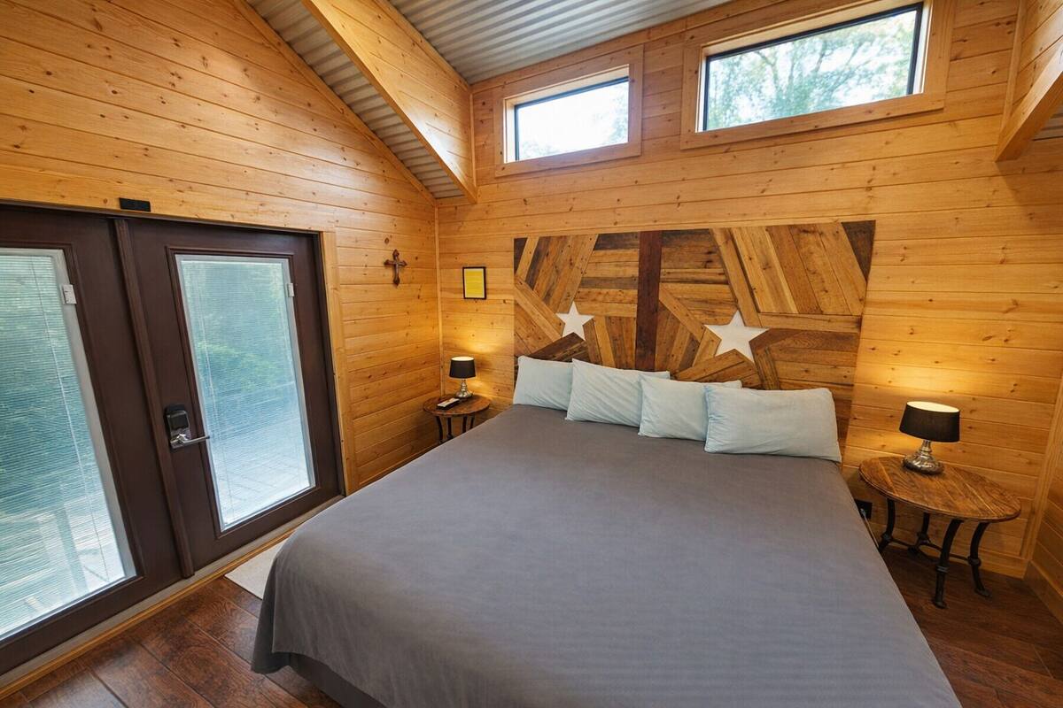 A wooden cabin bedroom with a bed, two bedside tables, star-shaped wall decoration, and a window.