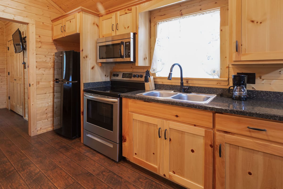 A wooden cabin-style kitchen with a stainless steel refrigerator, oven, and microwave.